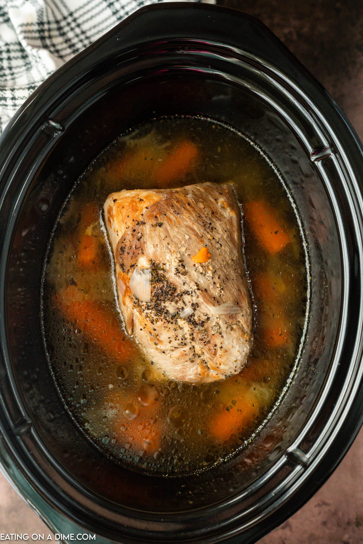The cooked pork roast in the crock pot with carrots and onions and gravy around the pork.  
