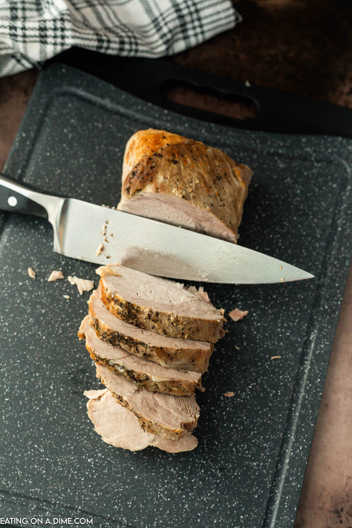 The pork roast being sliced on a cutting board.  
