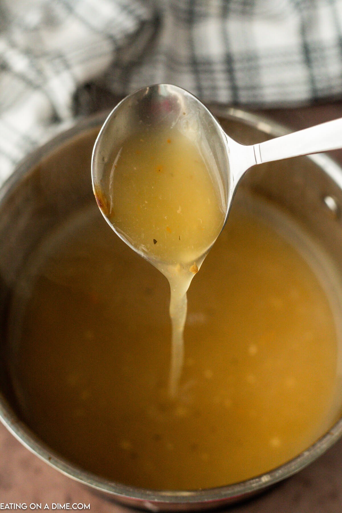 The pork roast gravy heated in a saucepan and thickened.  A gravy ladle spooning some of the mixture out of the saucepan and pouring it back into the pan.  