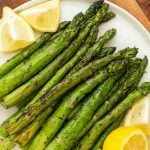A plate of roasted asparagus spears garnished with fresh lemon wedges, served on a white dish—perfect inspiration for your next grilled asparagus recipe.