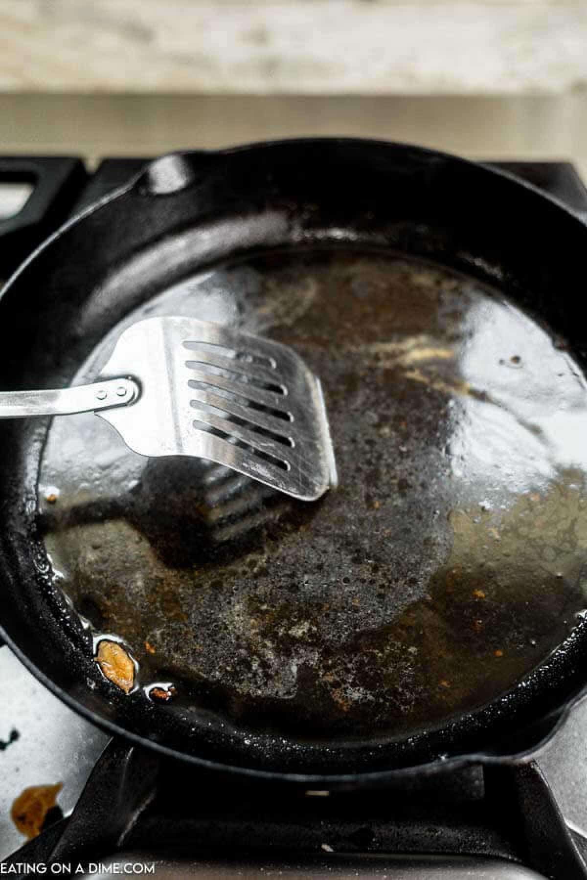 Scraping the food with a metal spatula on the cast iron skillet to clean