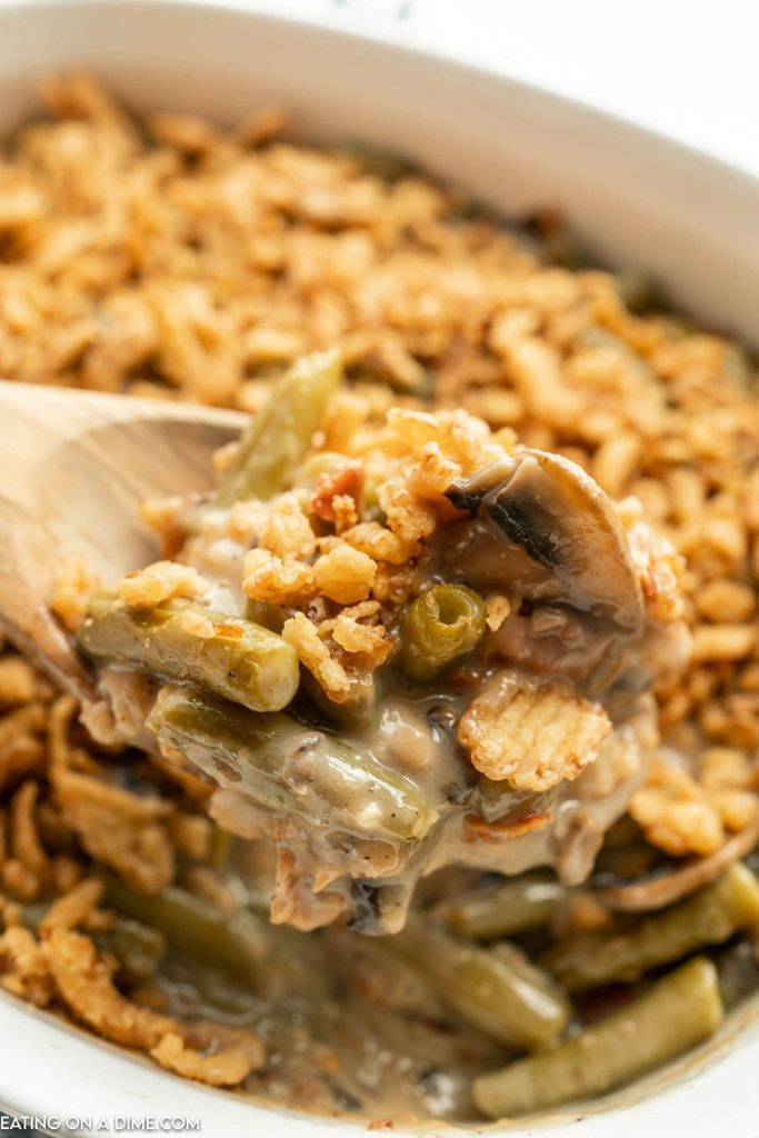 Green Bean Casserole with Bacon in baking dish with a serving on a wooden spoon