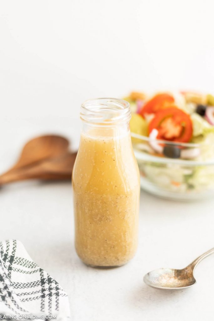 A jar of salad dressing with a bowl of salad in the background