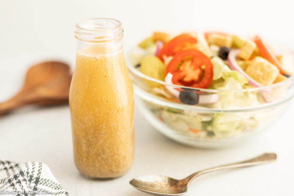 A jar of salad dressing with a bowl of salad in the background