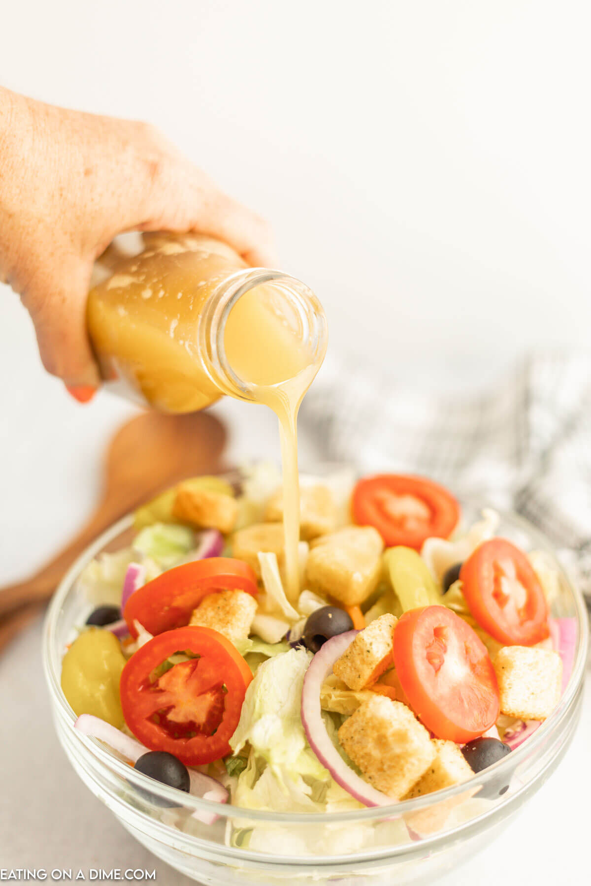 Pouring salad dressing over a bowl of salad. 