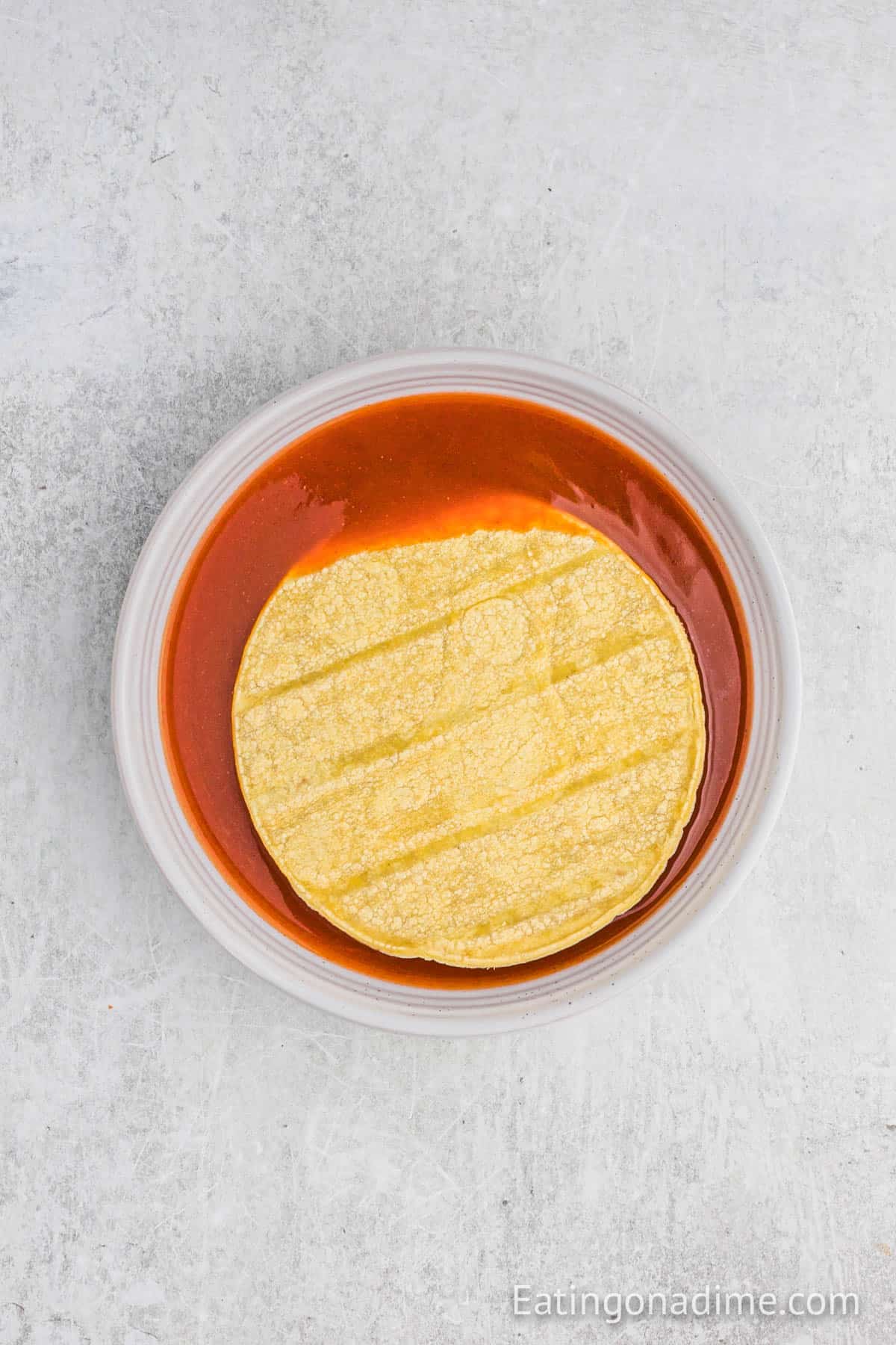 Corn tortillas in a bowl of enchilada sauce