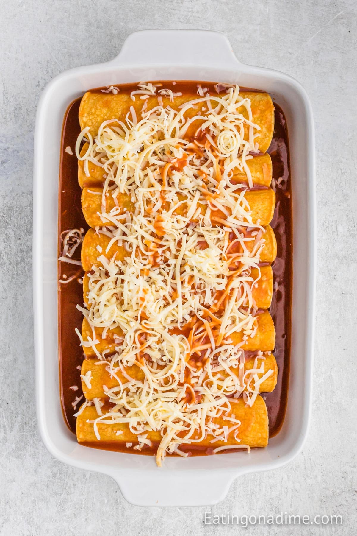 Enchilada placed in a baking dish with enchilada sauce. The prepared enchilada are topped with shredded cheese