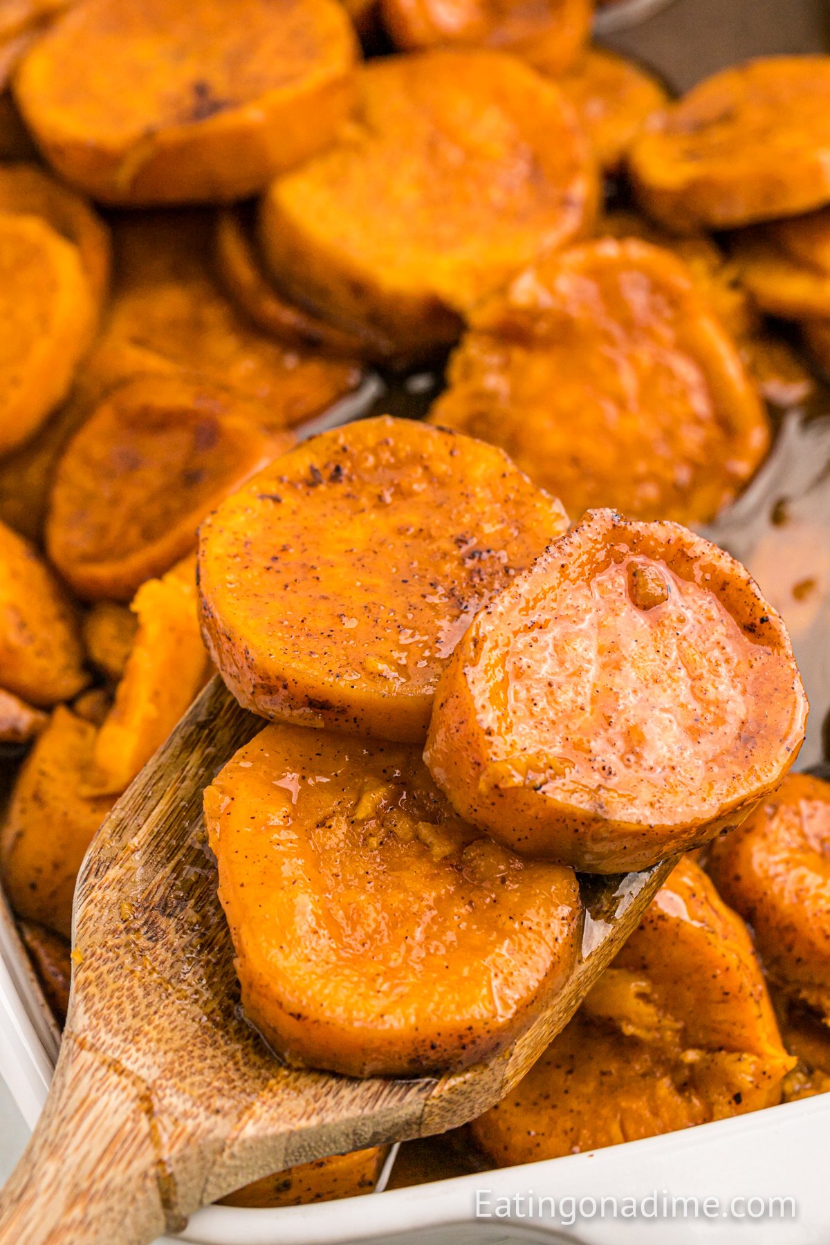 Candied sweet potatoes in a baking dish with a wooden spoon