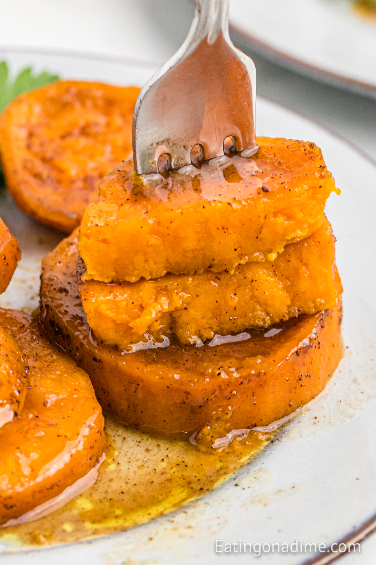 Candied sweet potatoes on a white plate with a serving on a fork