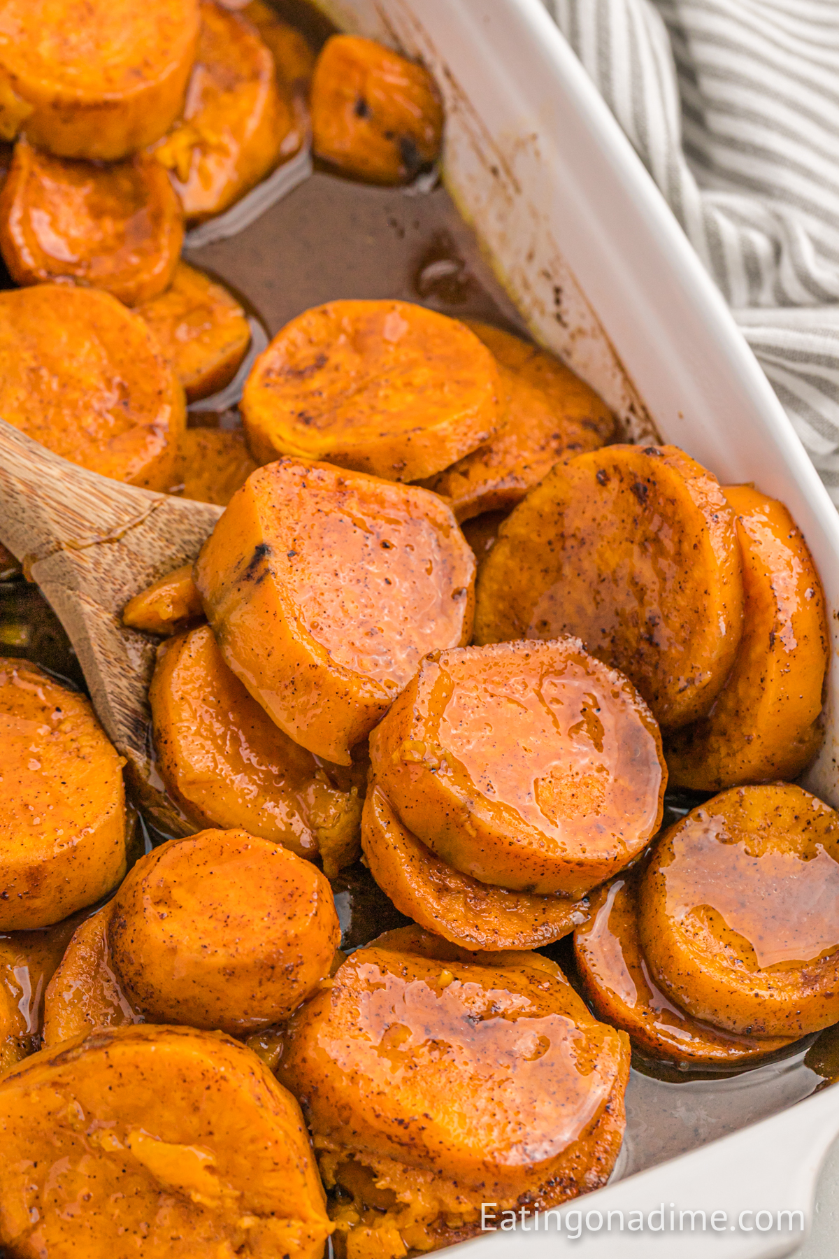 Candied sweet potatoes in a baking dish with a wooden spoon