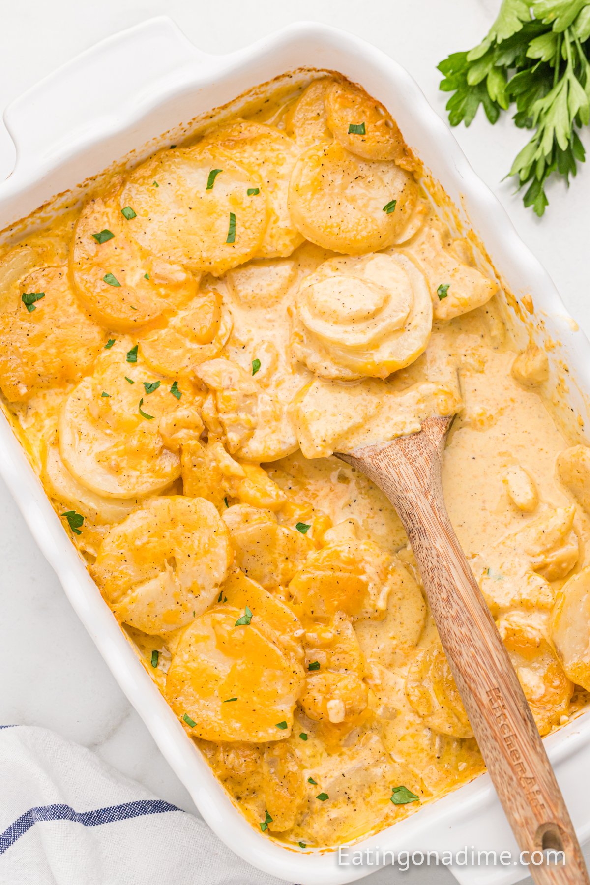 Scalloped potatoes in a baking dish with a wooden spoon