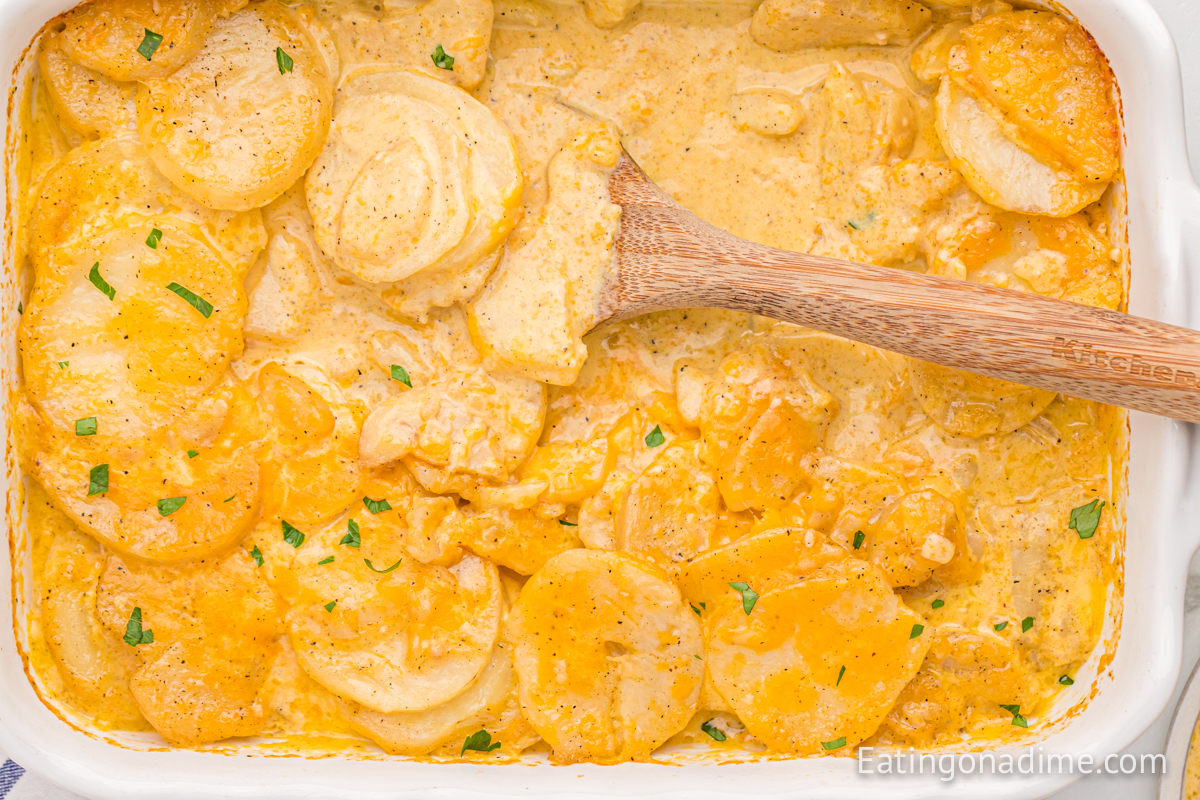 Scalloped potatoes in a baking dish with a wooden spoon