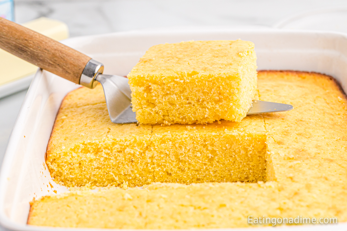 Sliced cornbread in a baking dish with a serving on a spatula