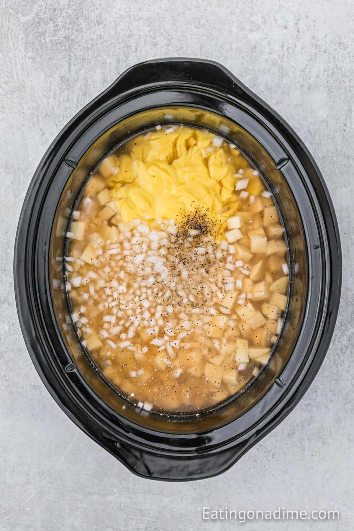 Diced potatoes, cream of chicken soup, diced onion and spices added to the slow cooker.