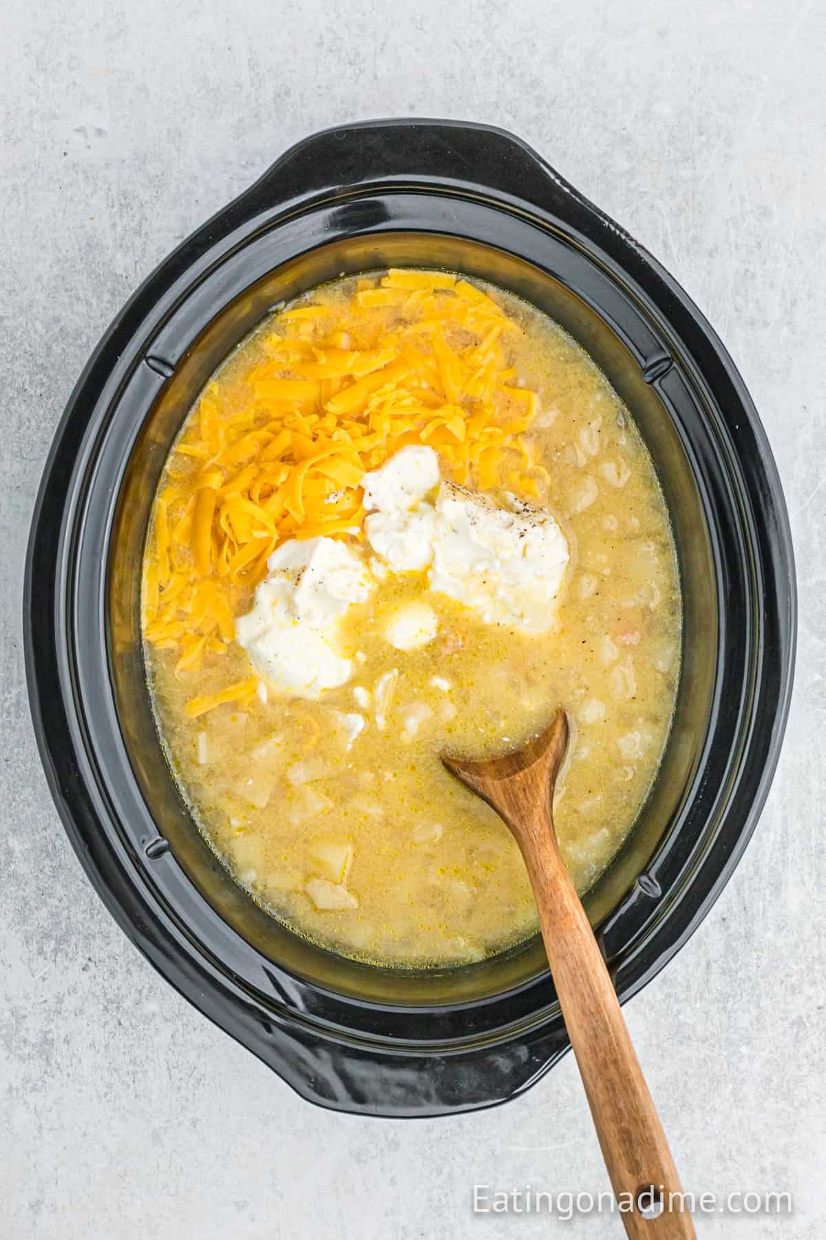 Shredded cheese and cream cheese is mixed into the potato mixture in the slow cooker.