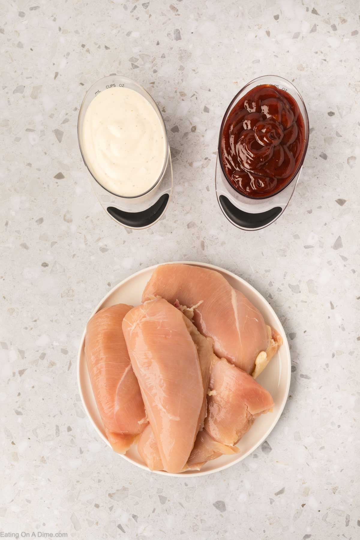 Chicken breast on a plate with a bowls of BBQ sauce and ranch dressing