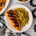 Grilled chicken and green beans on a white plate.