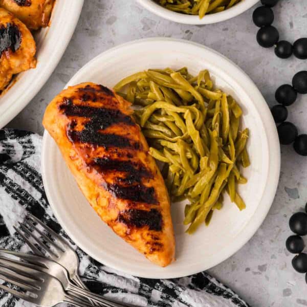 Grilled chicken and green beans on a white plate.