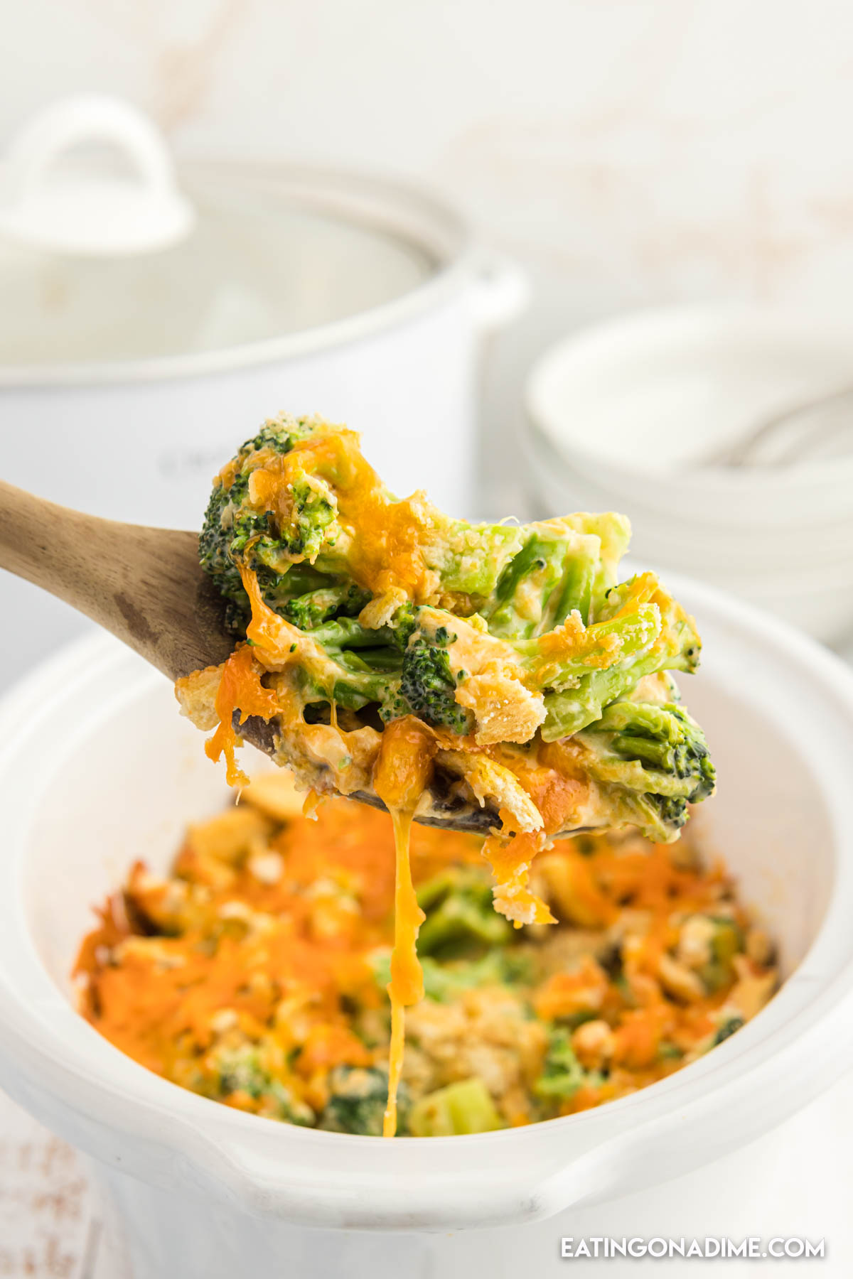 Broccoli Cheese Casserole in a white bowl with a serving on a wooden spoon