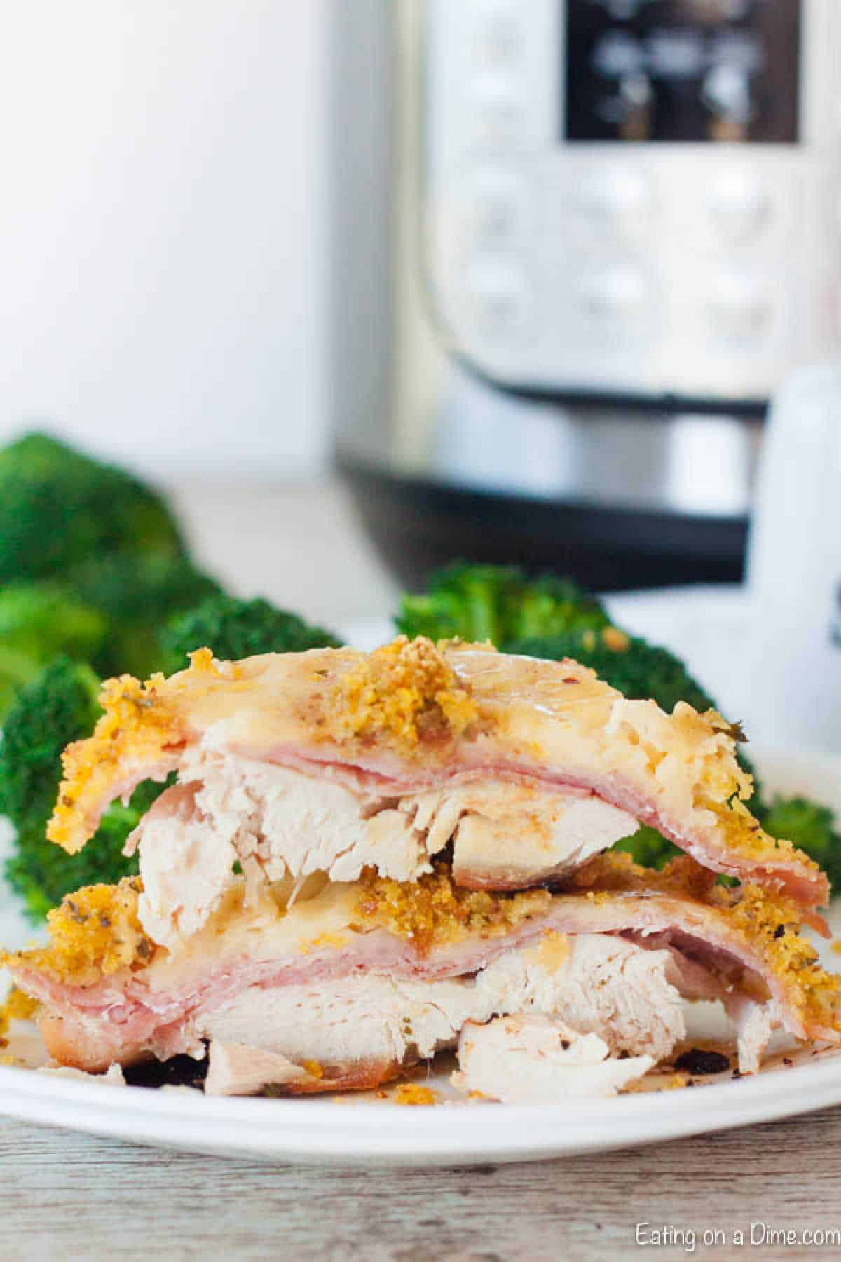 A sliced piece of chicken cordon bleu with ham and cheese stuffed inside, topped with a crispy breadcrumb layer, is elegantly plated. Fresh broccoli complements the dish, evoking flavors of an instant pot chicken cordon bleu recipe. A pristine white plate completes the presentation.