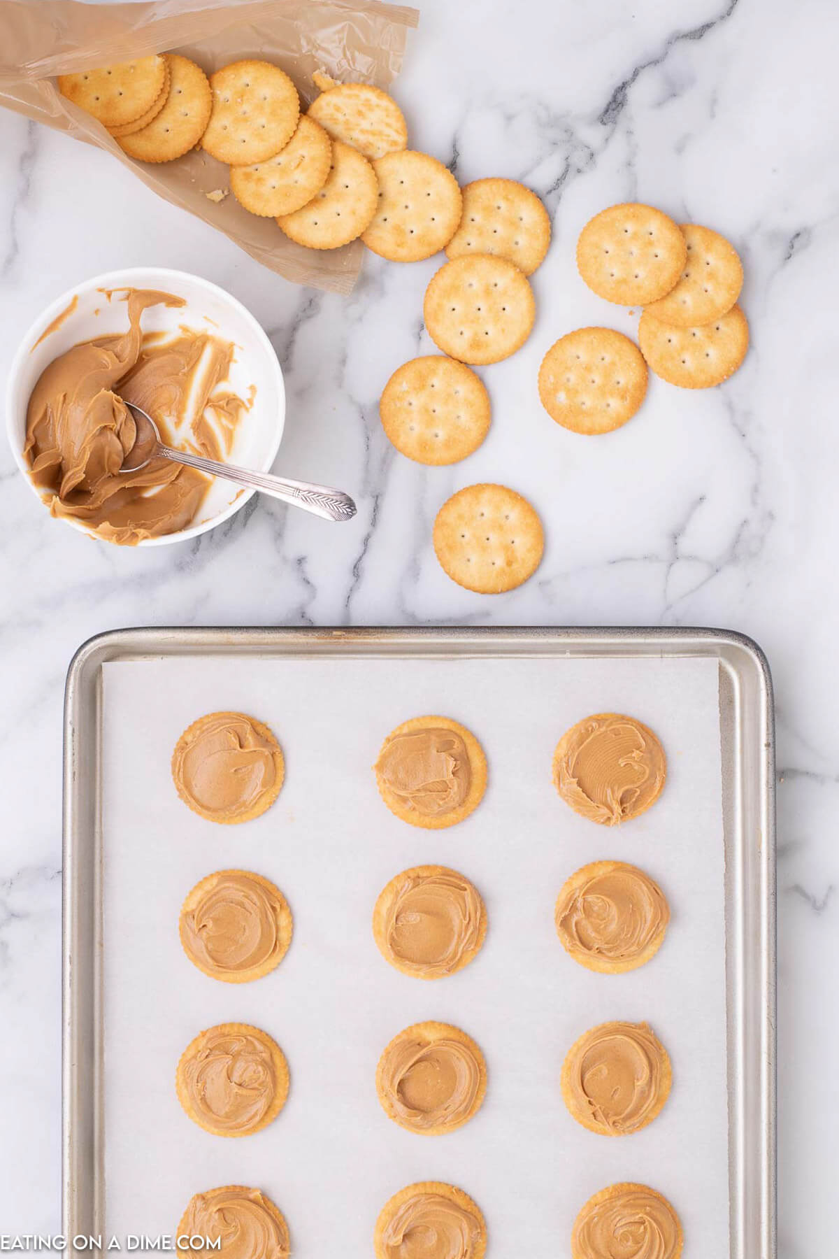 Ritz Crackers laid on a baking sheet lined with parchment paper with peanut butter spread on top of the crackers.  
