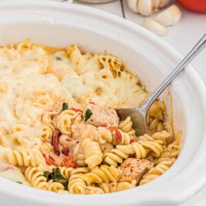 Close up image of red roasted chicken pasta in a slow cooker with a spoon