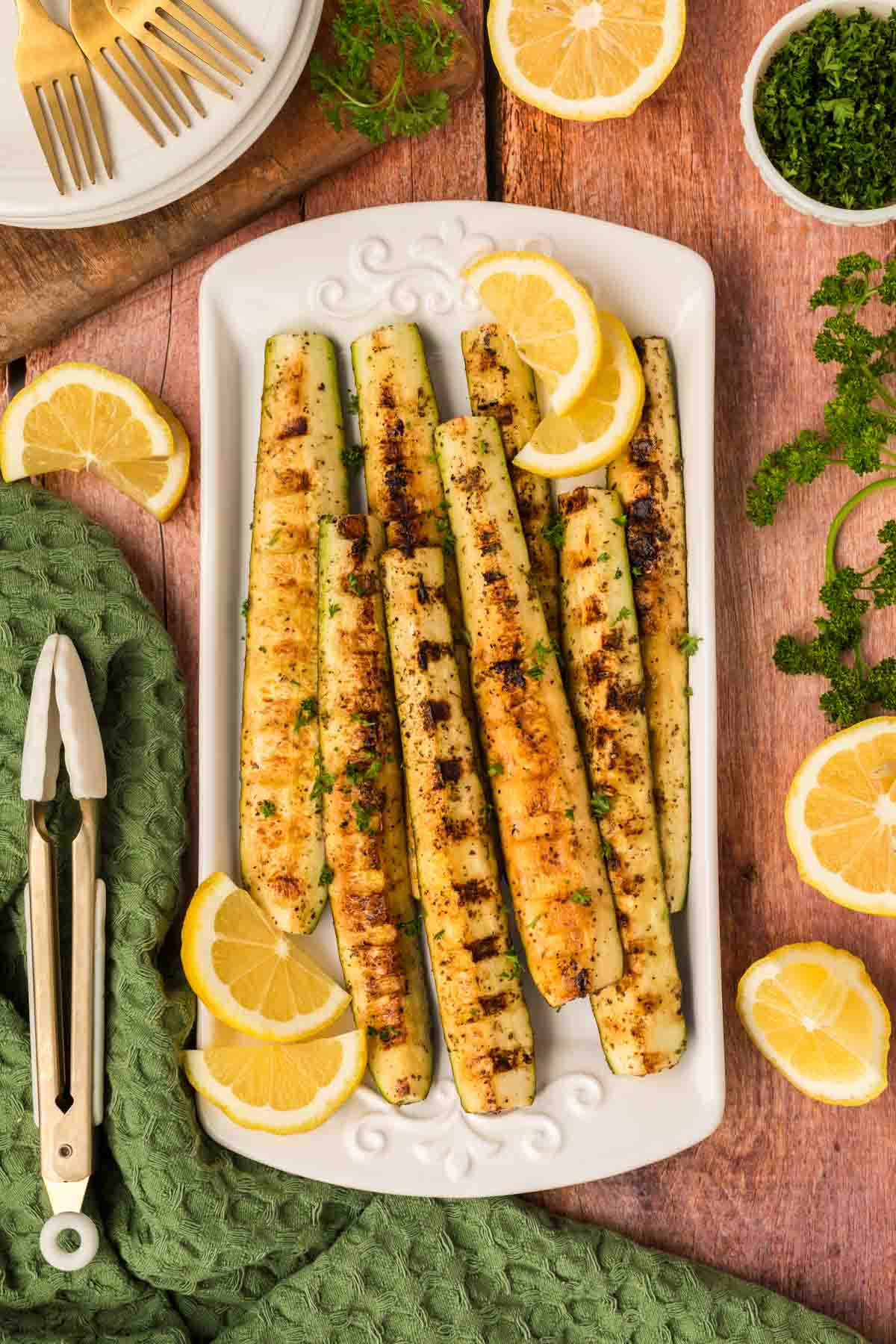 Grilled zucchini spears on a platter with fresh lemon slices