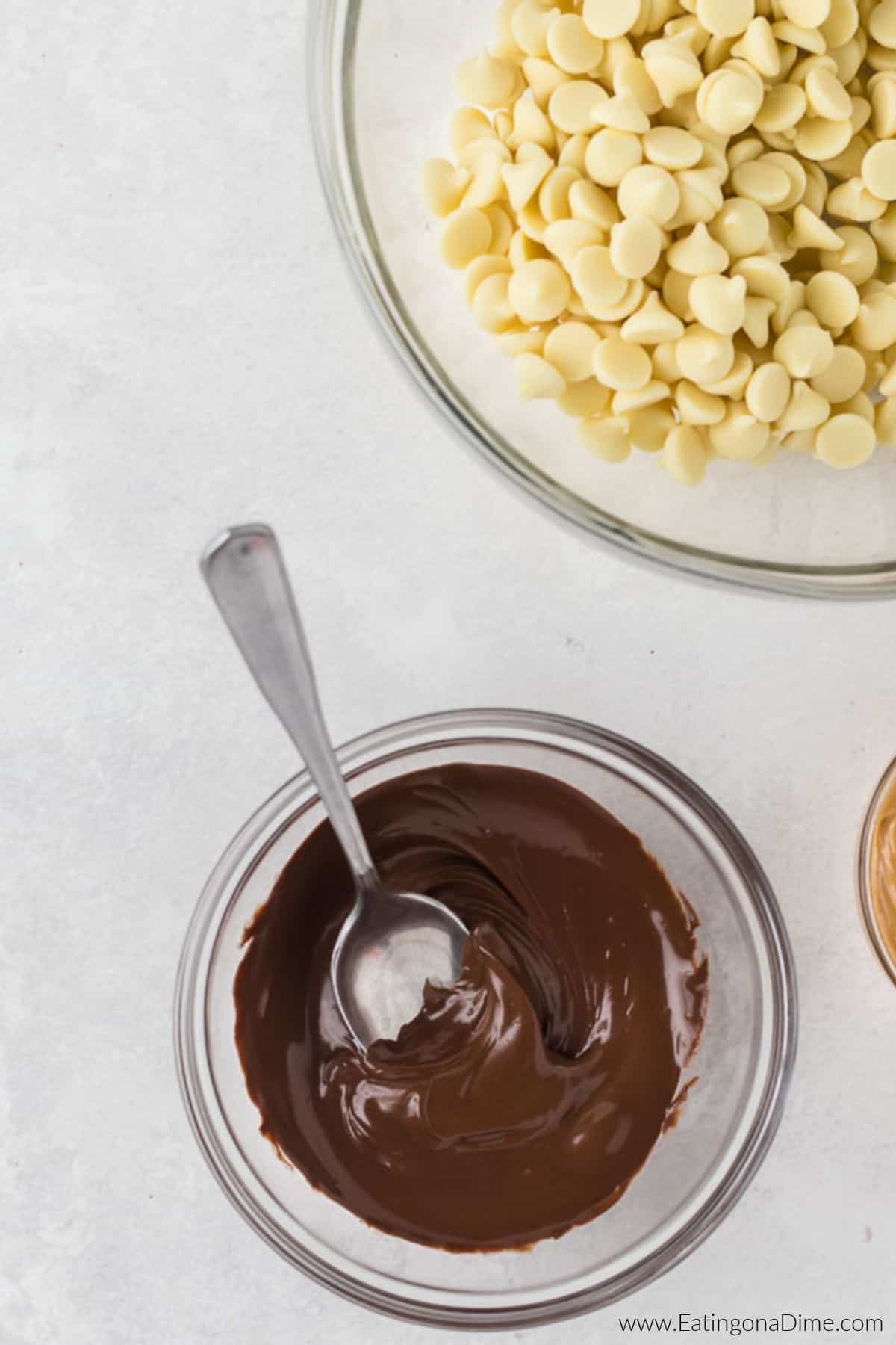 Melted chocolate in a bowl with the vanilla chips in a bowl nearby.