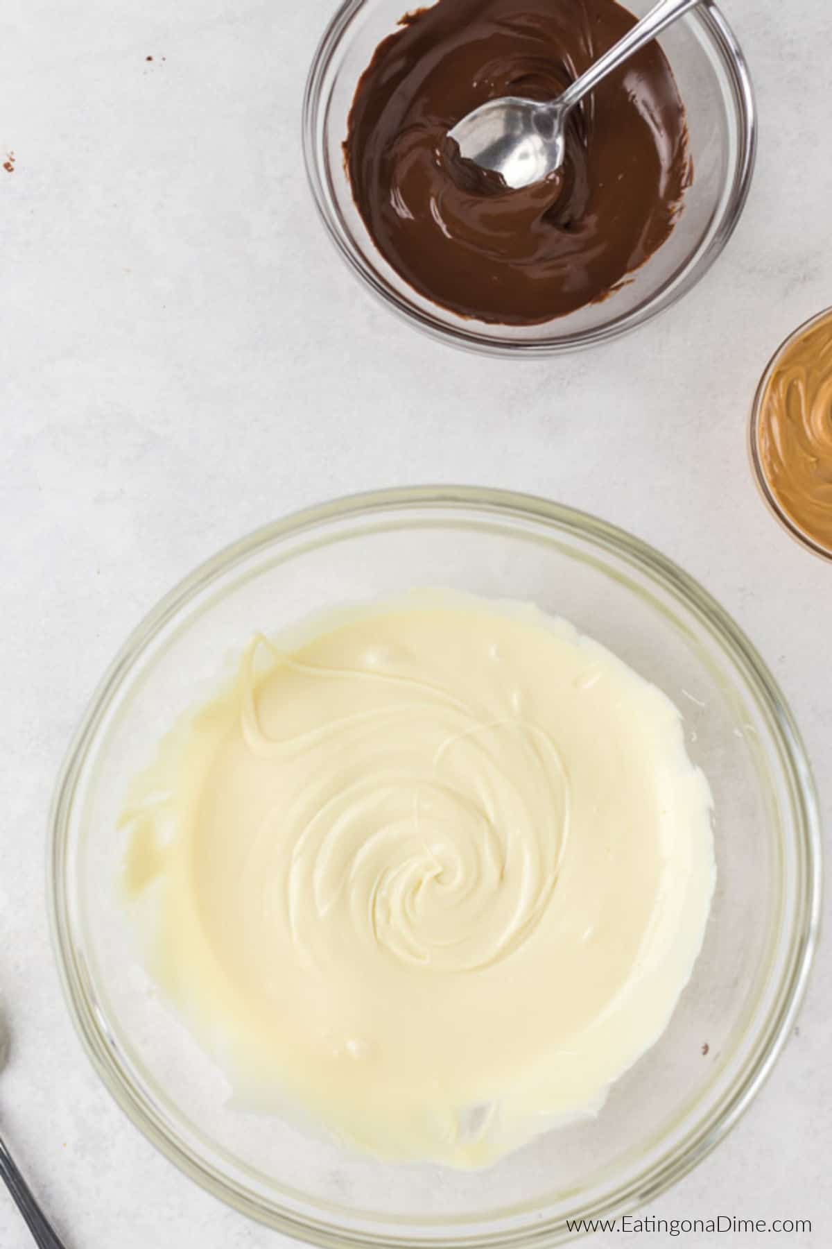 Melted vanilla chips in a bowl with a bowl of melted chocolate nearby.