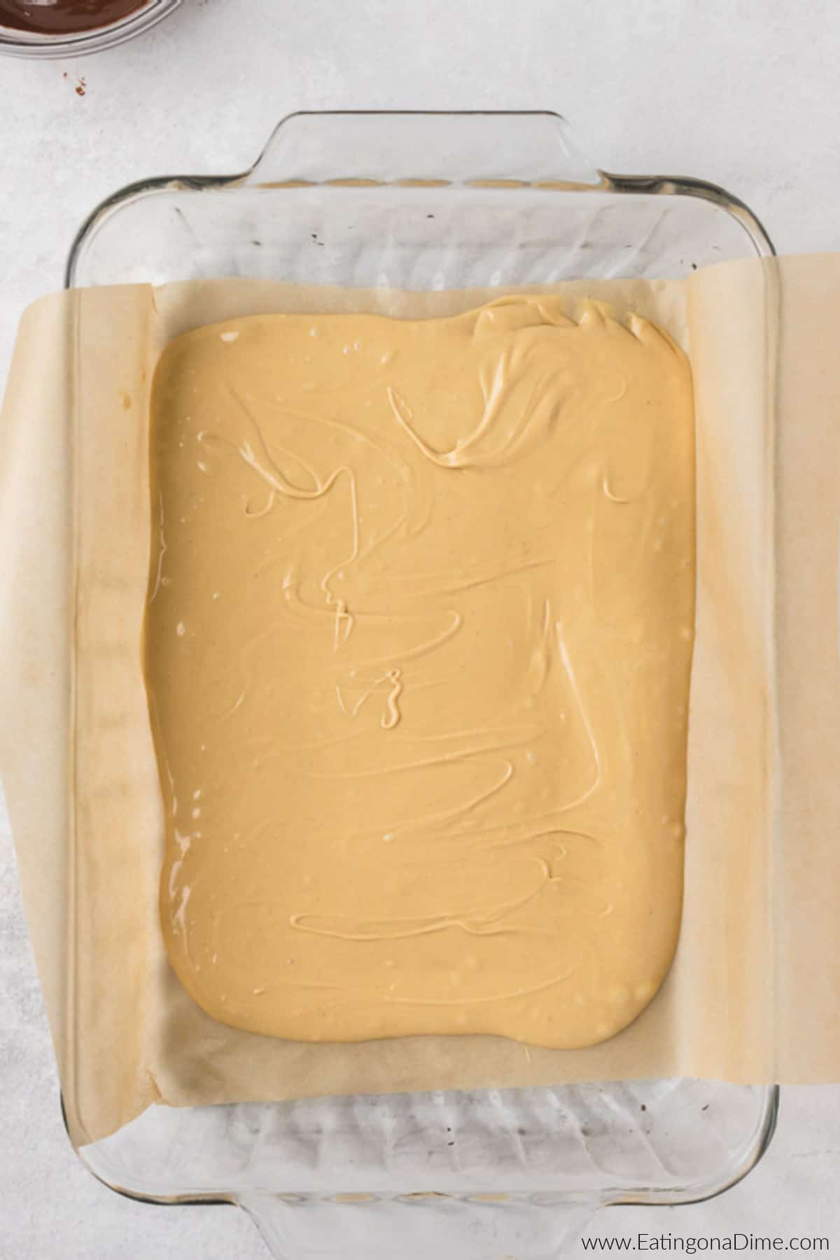 Vanilla and peanut butter mixture poured into a glass baking dish lined with parchment paper.