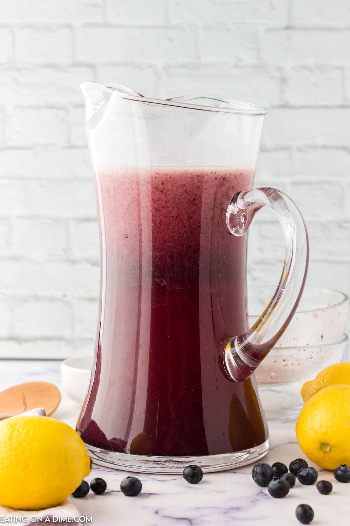 Blueberry Lemonade in a glass pitcher with fresh lemons on the side