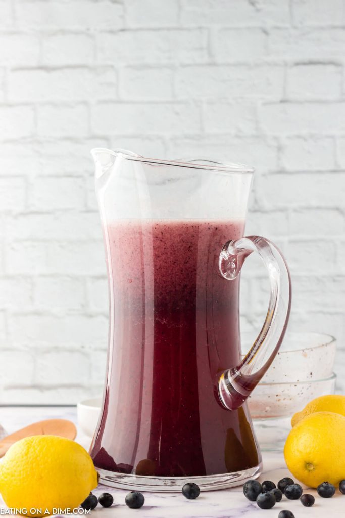 Blueberry Lemonade in a glass pitcher with fresh lemons on the side