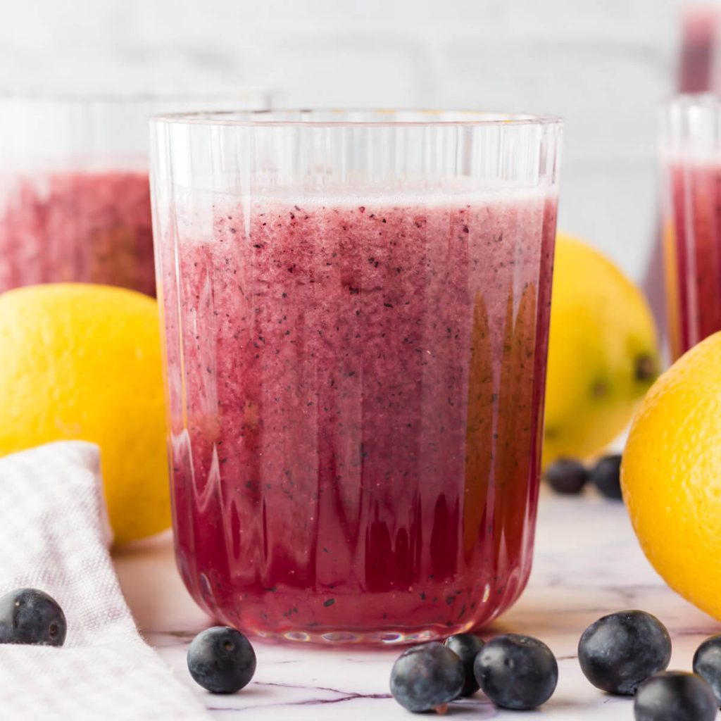 Blueberry Lemonade in a glass with fresh lemons on the side