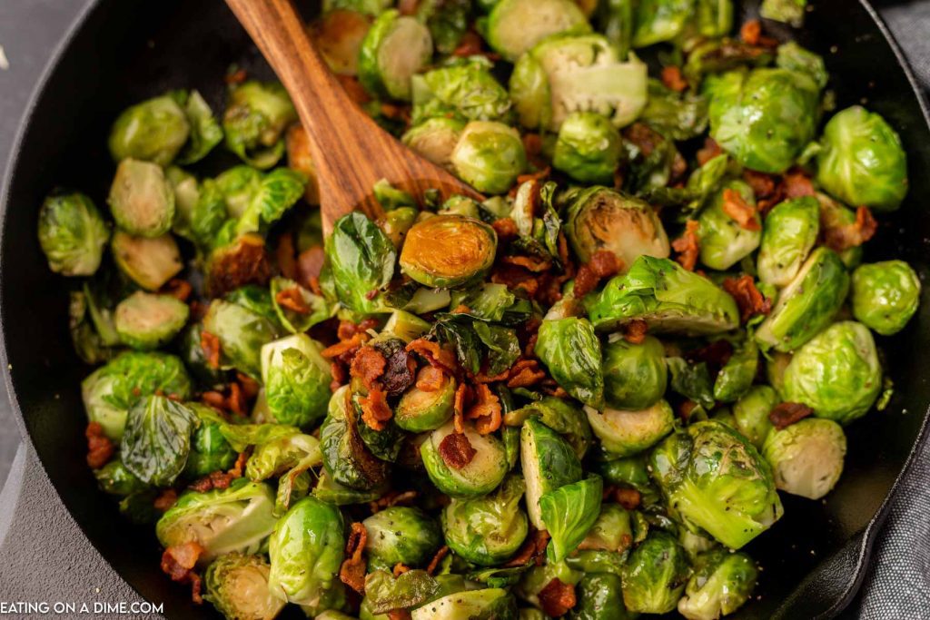Close up image of bacon brussel sprouts on a black plate with a wooden spoon