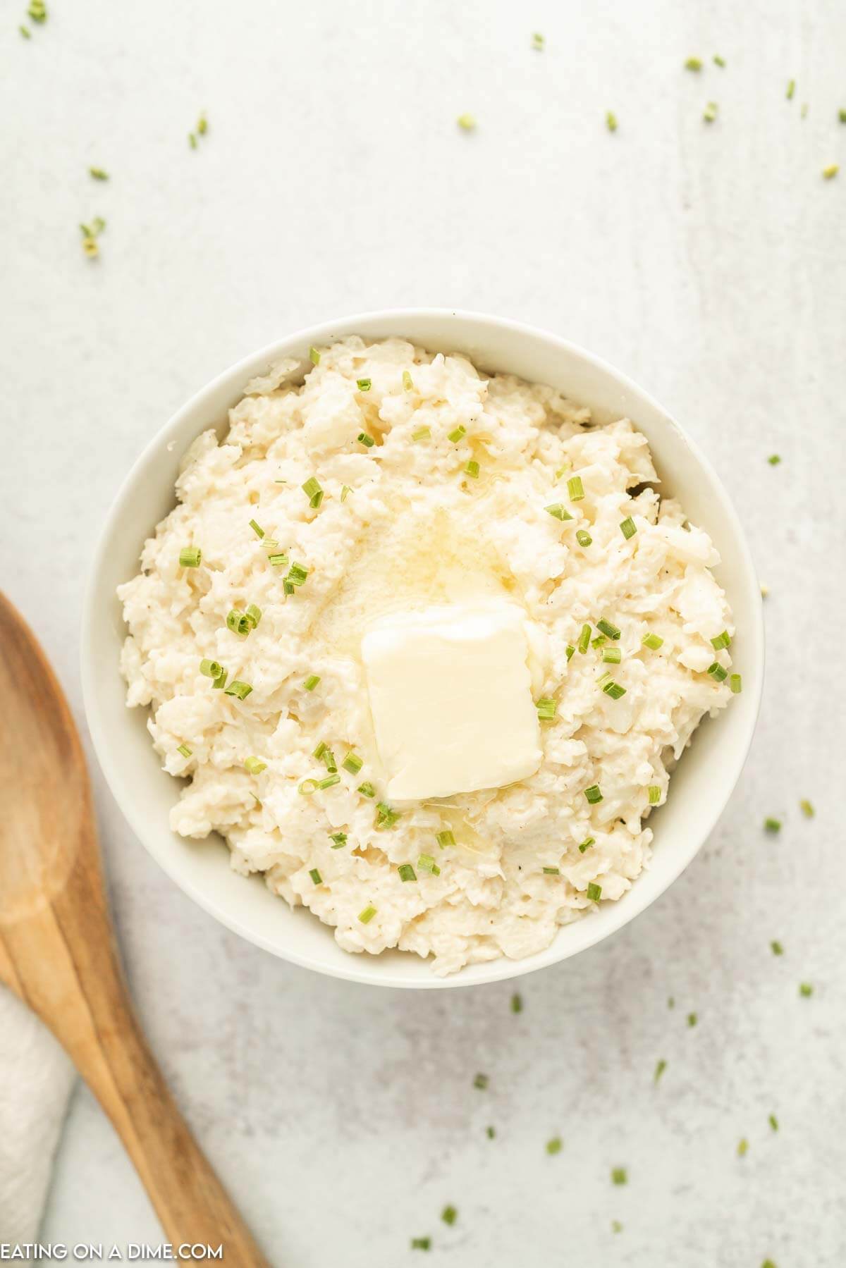 Close up image of mashed cauliflower with butter on top in a bowl with a wooden spoon