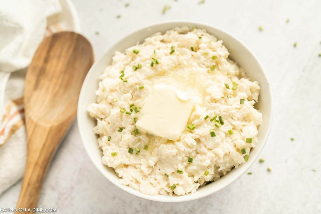 Close up image of mashed cauliflower with butter on top in a bowl with a wooden spoon