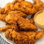 Close up of chicken tenders on a white plate with a small bowl of Chick-fil-A sauce next to it.