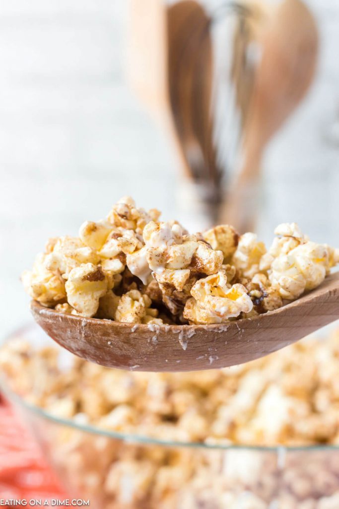 Cinnamon Roll Popcorn in a clear bowl with a serving on a wooden spoon