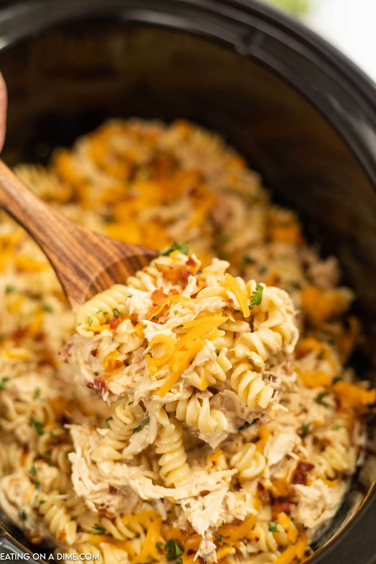 Chicken bacon ranch pasta in a crock pot with a serving on a wooden spoon