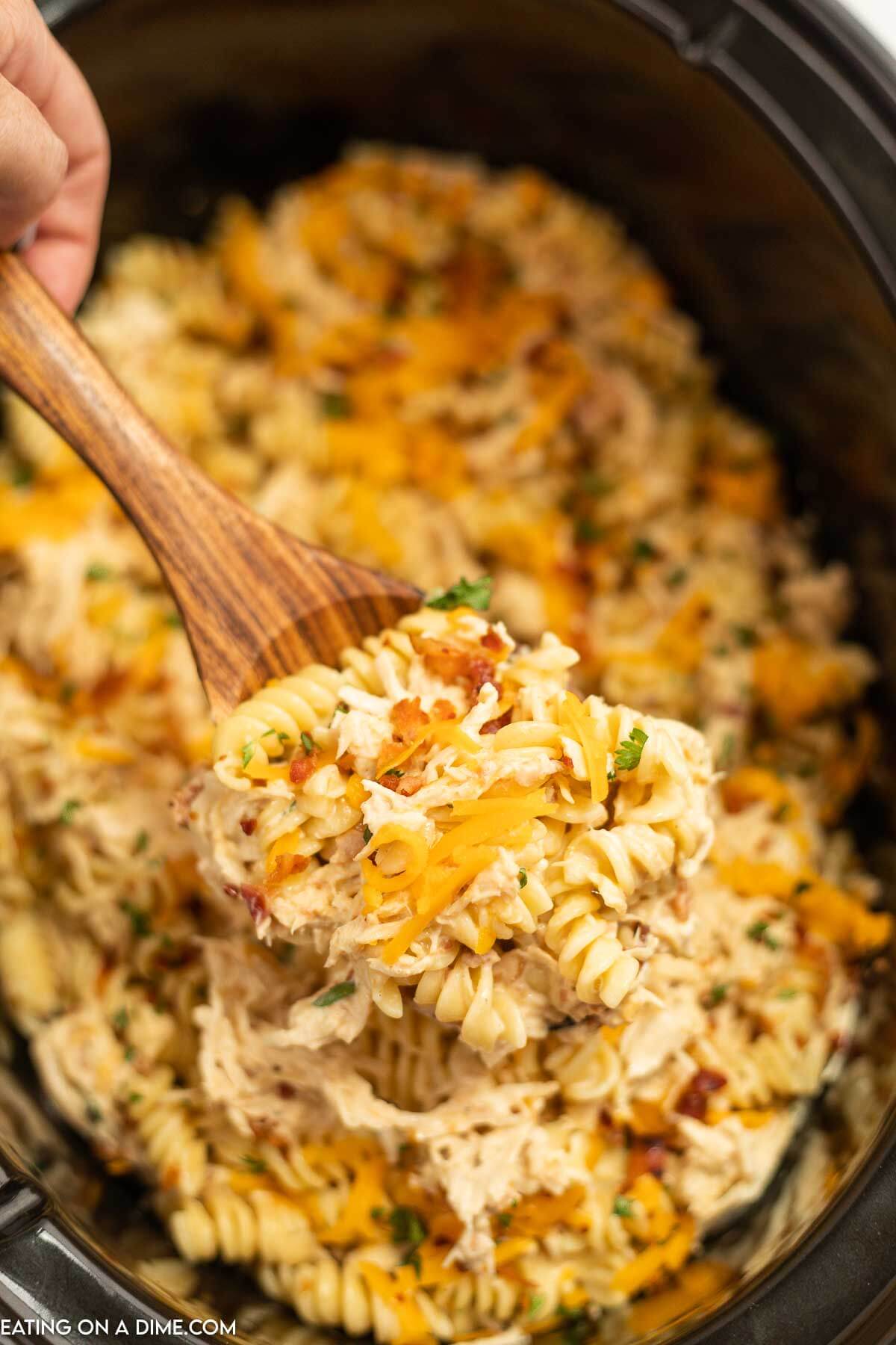 Chicken bacon ranch pasta in a crock pot with a serving on a wooden spoon