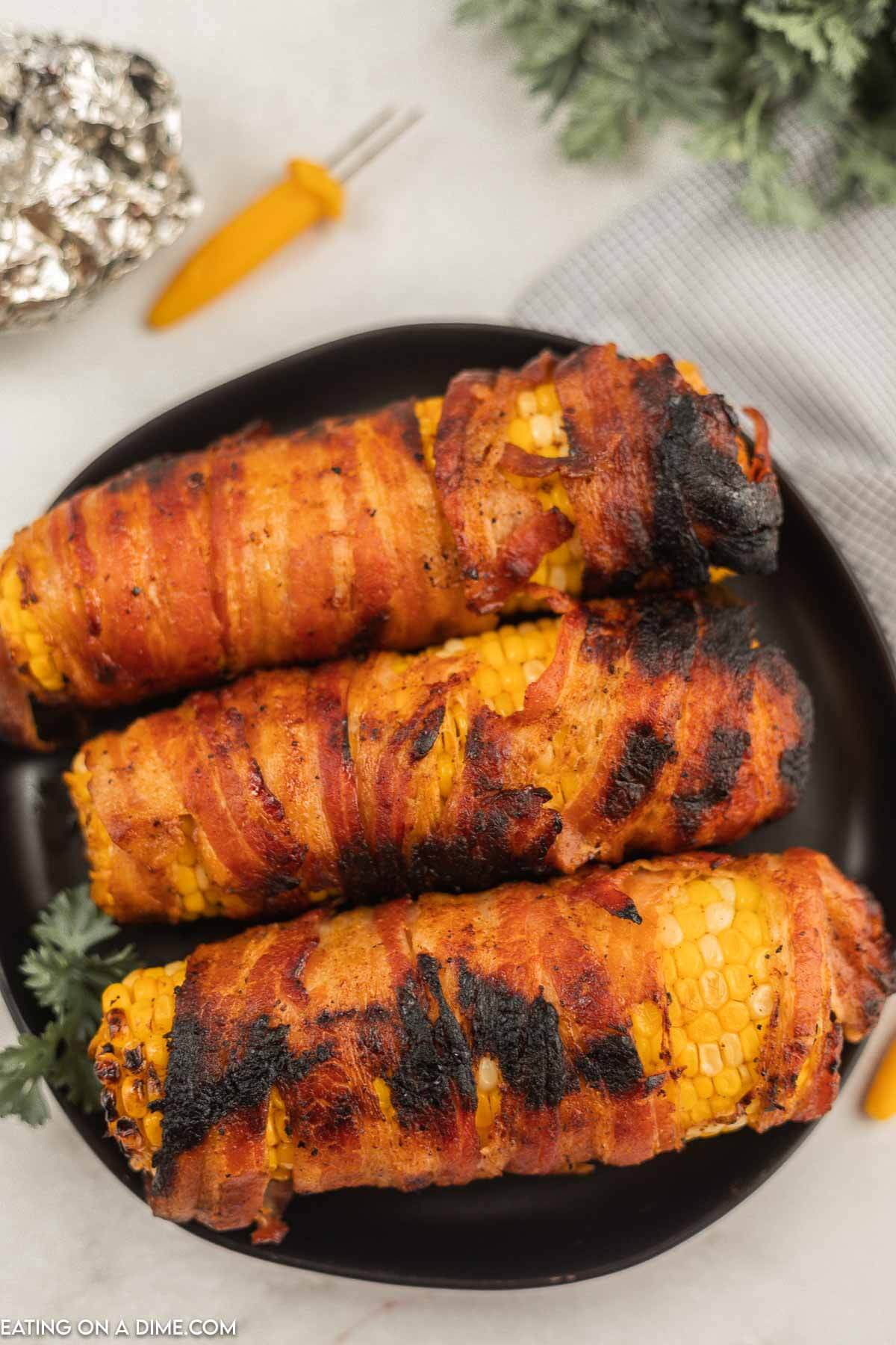 bacon wrapped corn on the cob on a black plate