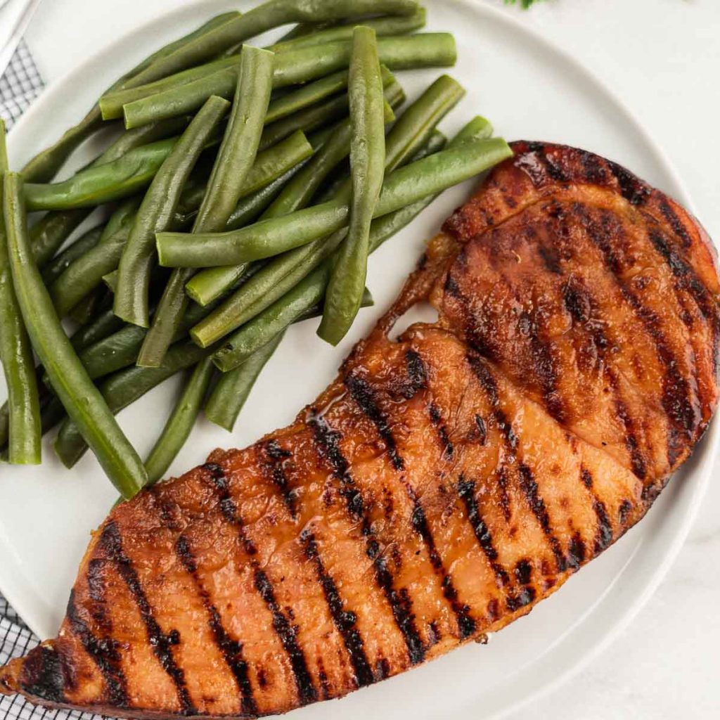 Grilled ham steak on a white plate with green beans.