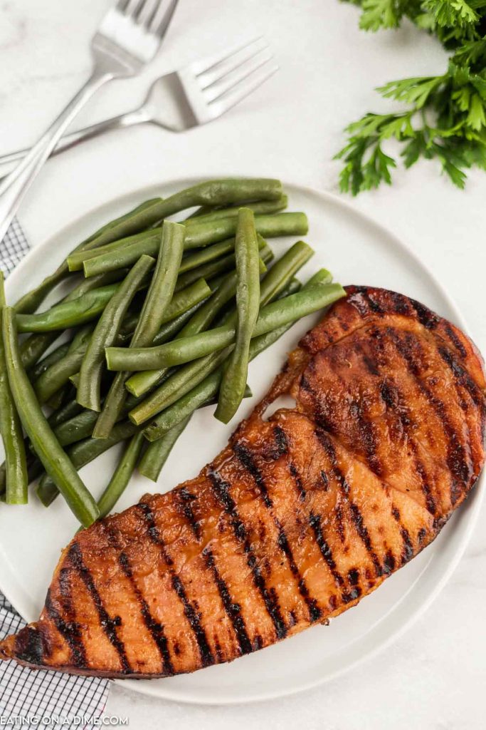 Grilled ham steak on a white plate with green beans.