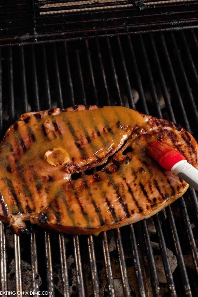 Ham steak on the grill being basted. 