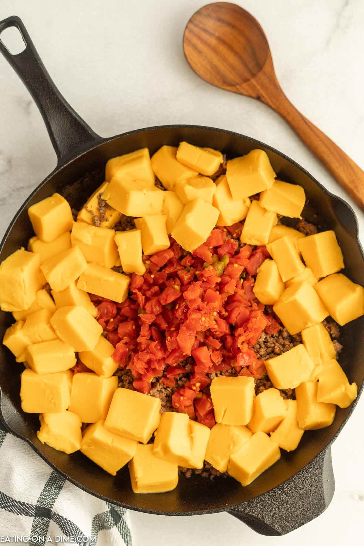 Velveeta Cubes in a cast iron skillet topped with Rotel and ground beef