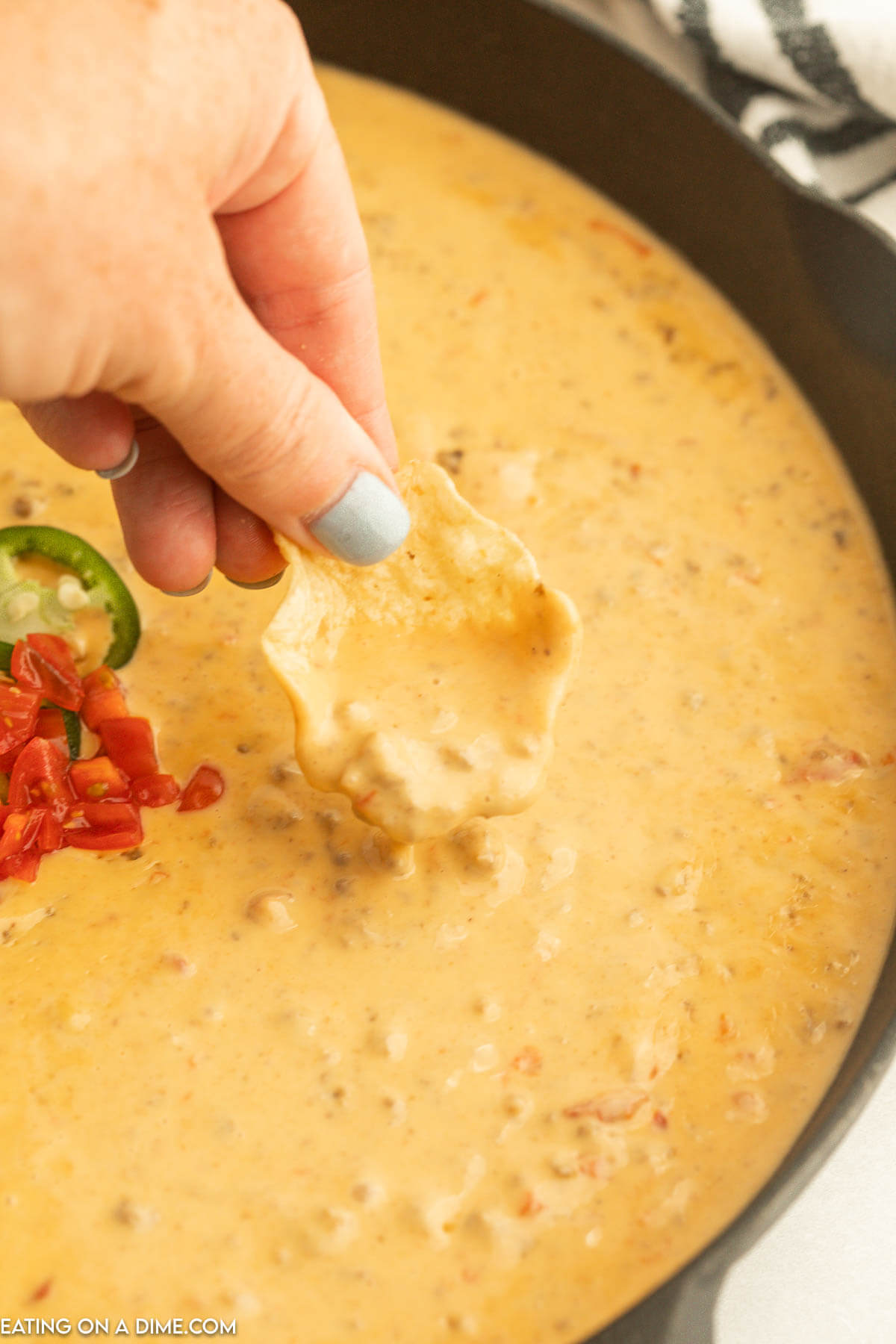 Rotel Dip in a cast iron skillet with a chip being dipped in
