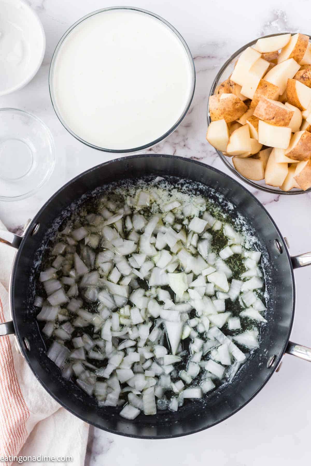 Chopped onions with melted butter in a large pot with diced raw potatoes and milk in small bowls nearby.