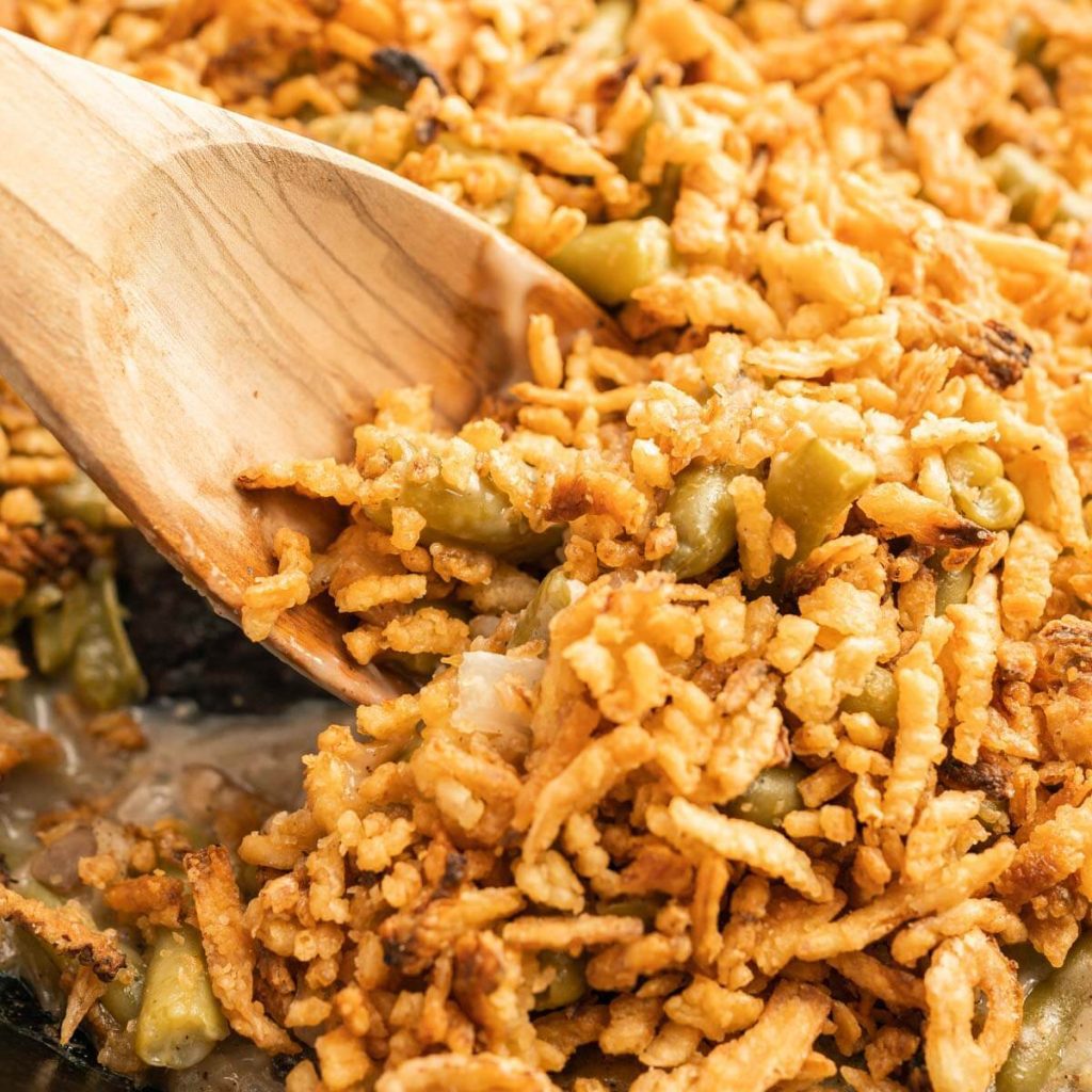 skillet green bean casserole and a serving on a wooden spoon