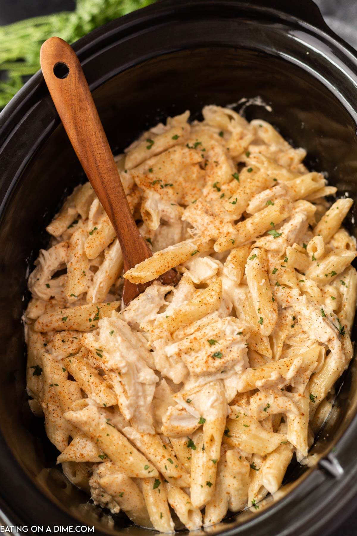 Cajun chicken pasta in the slow cooker with a wooden spoon