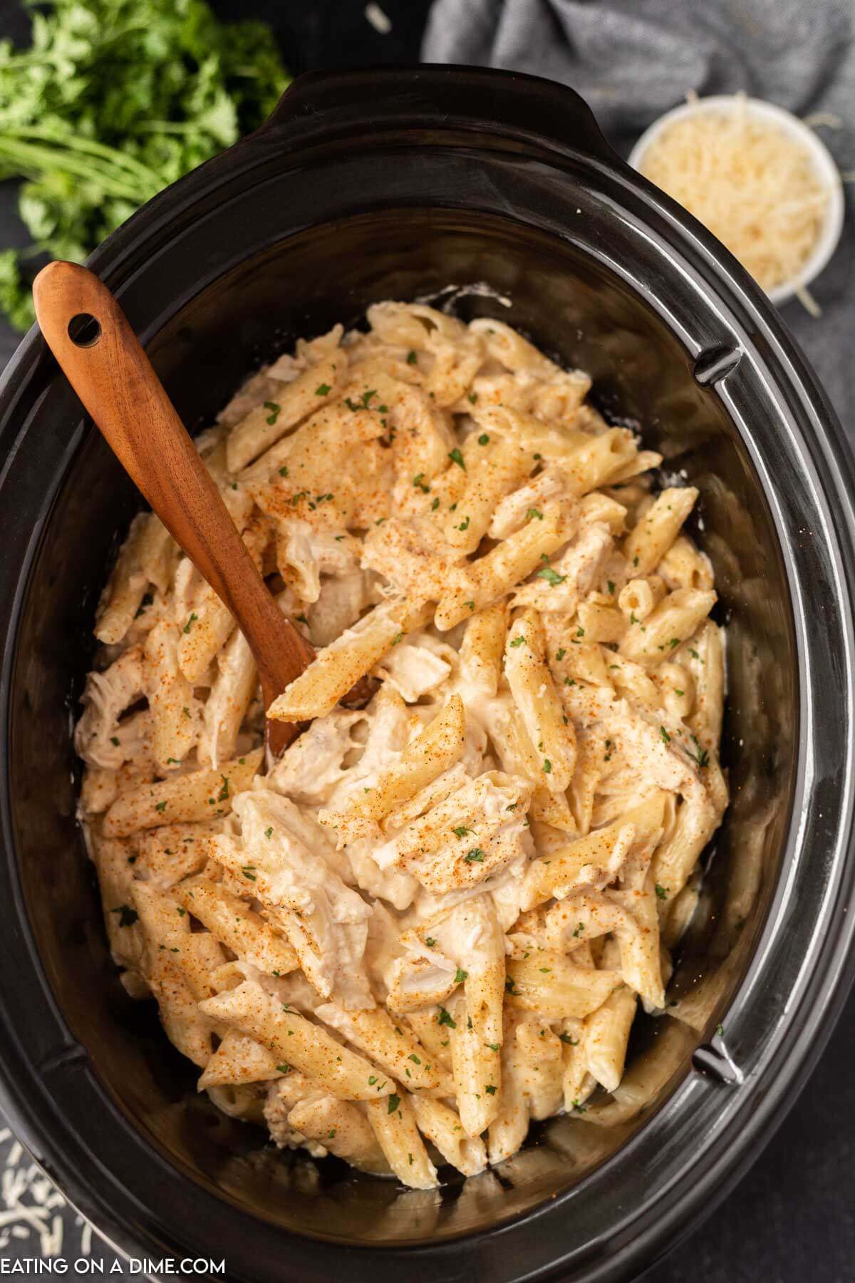 Cajun chicken pasta in the slow cooker with a wooden spoon